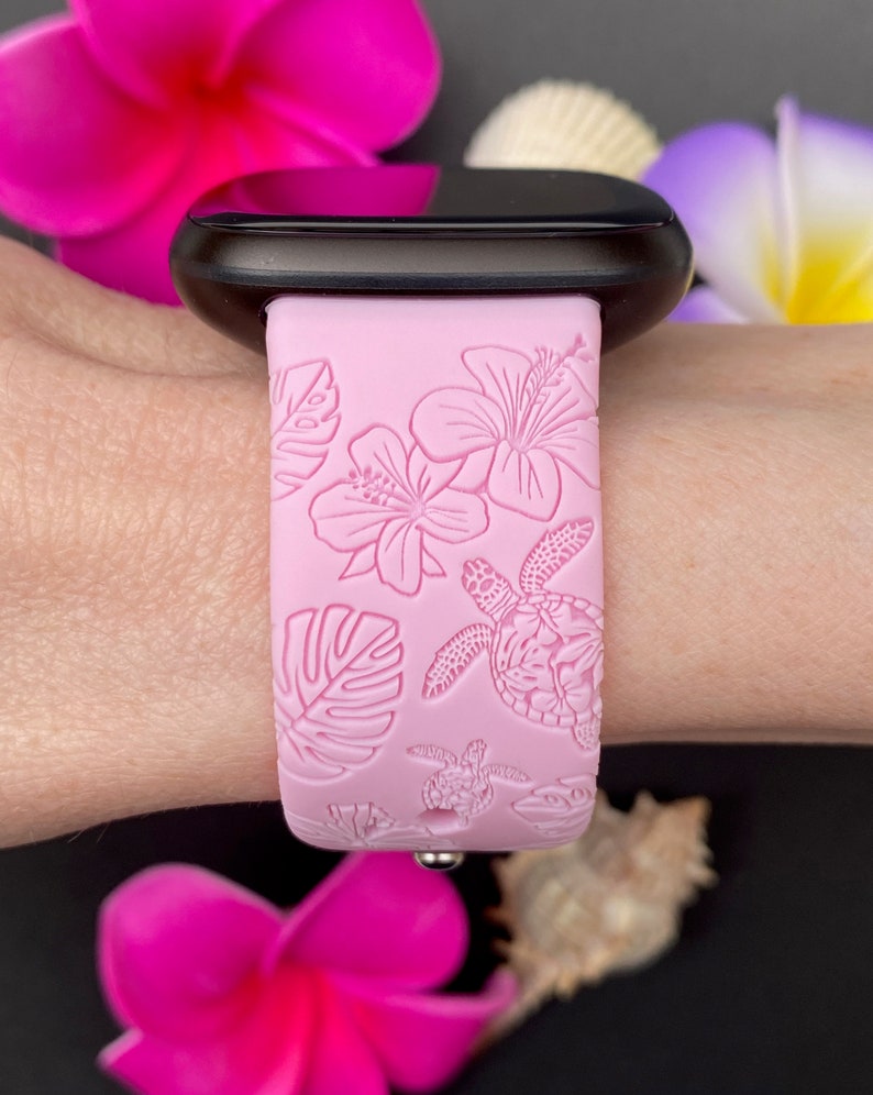 May include: Pink silicone watch strap with a tropical floral and sea turtle design. The strap is shown on a wrist.