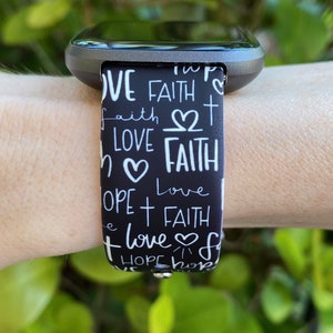 K&ouml;nnte beinhalten: Schwarz-wei&szlig;es Armband f&uuml;r eine Uhr mit den Worten "Love", "Faith" und "Hope", die sich in einem Muster wiederholen. Das Armband hat ein wei&szlig;es Herz- und Kreuzdesign.