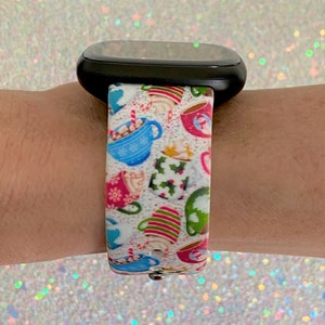 Puede incluir: Una correa de reloj blanca con un dise&ntilde;o navide&ntilde;o con tazas coloridas con chocolate caliente y bastones de caramelo.
