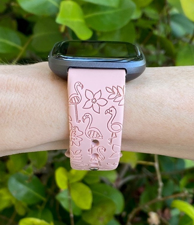 May include: A pink silicone watch band with a flamingo and floral pattern. The band is designed for a smart watch.