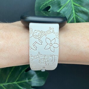 May include: White silicone watch band with a sloth and floral design. The band is compatible with smartwatches.