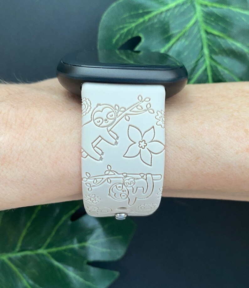 May include: White silicone watch band with a sloth and floral design. The band is compatible with smartwatches.