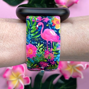 May include: A pink flamingo and tropical floral print watch band for a smartwatch. The band is made of silicone and has a navy blue background.
