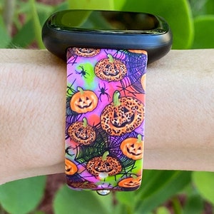 May include: A pink, black, green, and orange watch band with a pattern of pumpkins and spiderwebs. The pumpkins have a leopard print design.