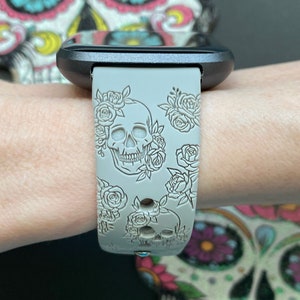 K&ouml;nnte beinhalten: Ein graues Silikon-Armband mit Totenkopf- und Blumenmuster. Das Armband ist mit einem Totenkopf und Rosen gepr&auml;gt.