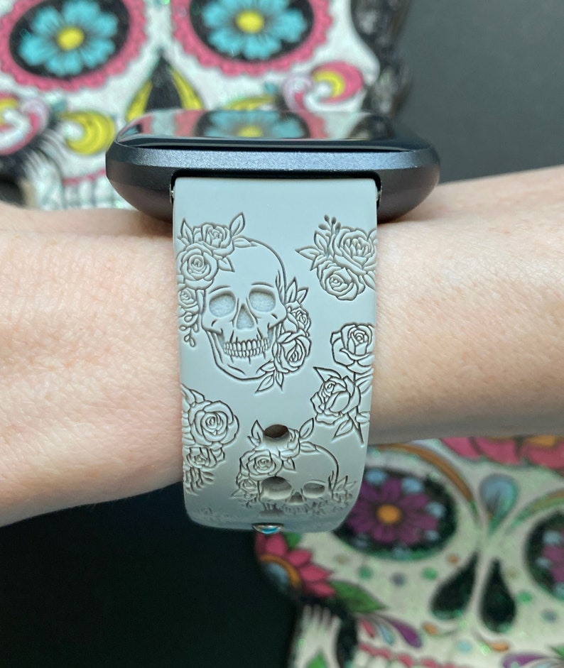 K&ouml;nnte beinhalten: Ein graues Silikon-Armband mit Totenkopf- und Blumenmuster. Das Armband ist mit einem Totenkopf und Rosen gepr&auml;gt.