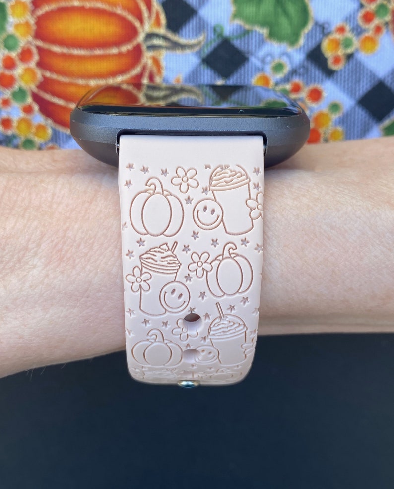 May include: A pink silicone watch band with a pattern of pumpkins, coffee cups, and stars. The band is designed for a smartwatch.