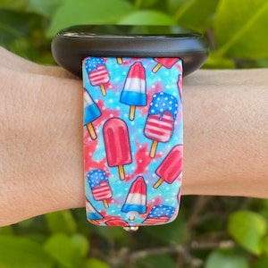 May include: A blue and red patterned watch band with a design of ice cream pops with American flag colors. The band is made of silicone and is compatible with smartwatches.