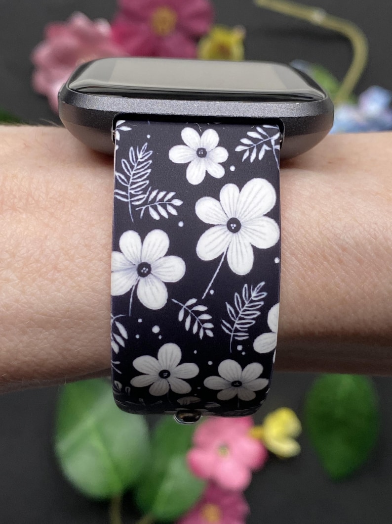 May include: Black smartwatch band with a white floral pattern. The band features a repeating design of large flowers and smaller leaves on a dark background. The watch face is black.