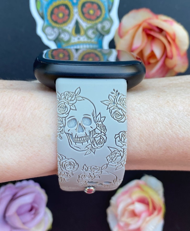 May include: A grey silicone watch band with a white skull and rose design. The band is on a person's wrist.