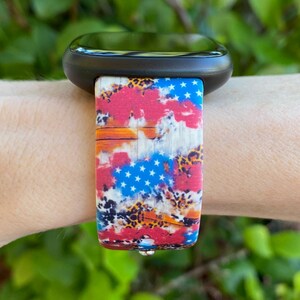 Pu&ograve; includere: Uno smartwatch nero con un cinturino colorato che presenta un design a bandiera americana rosso, bianco e blu con un motivo a stampa leopardata.