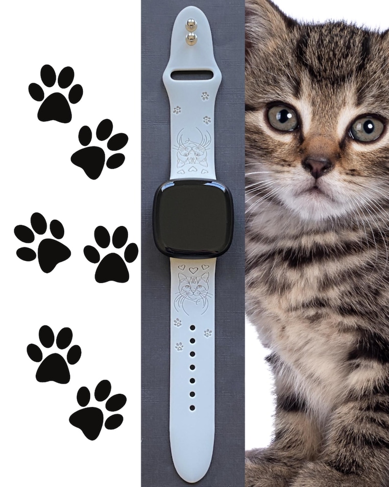 May include: A light gray smartwatch band with a black screen, featuring a cat face design and paw prints. The band is next to a tabby kitten and black paw print decals.