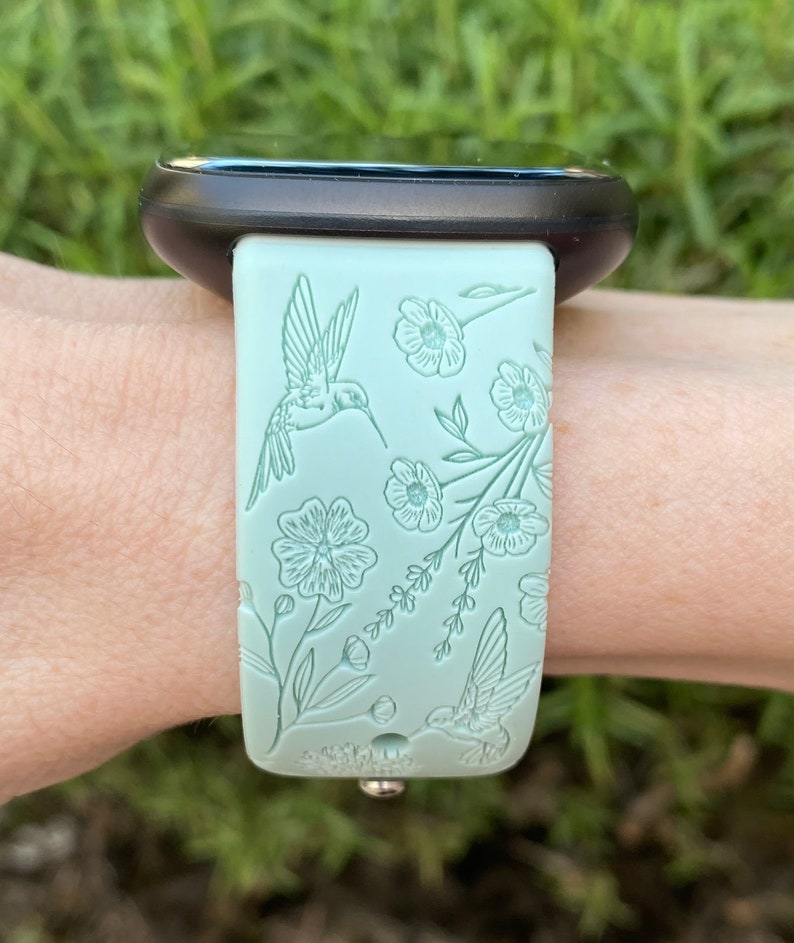 May include: A light green silicone watch strap with a floral and hummingbird design.