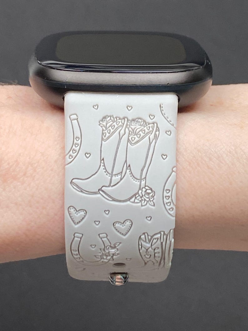 May include: White silicone watch band with a design of cowboy boots, hearts, and horseshoes. The band is compatible with a smartwatch.