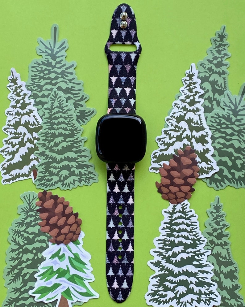 May include: A black and white patterned watch band with a black watch face. The band features a repeating pattern of small green Christmas trees. The watch is surrounded by green Christmas tree stickers.