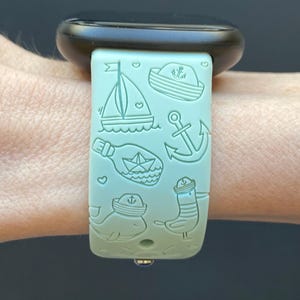 May include: A light blue watch strap with a nautical theme. The strap features a sailboat, an anchor, a bottle with a message in it, a whale, a seagull, and a sailor hat.