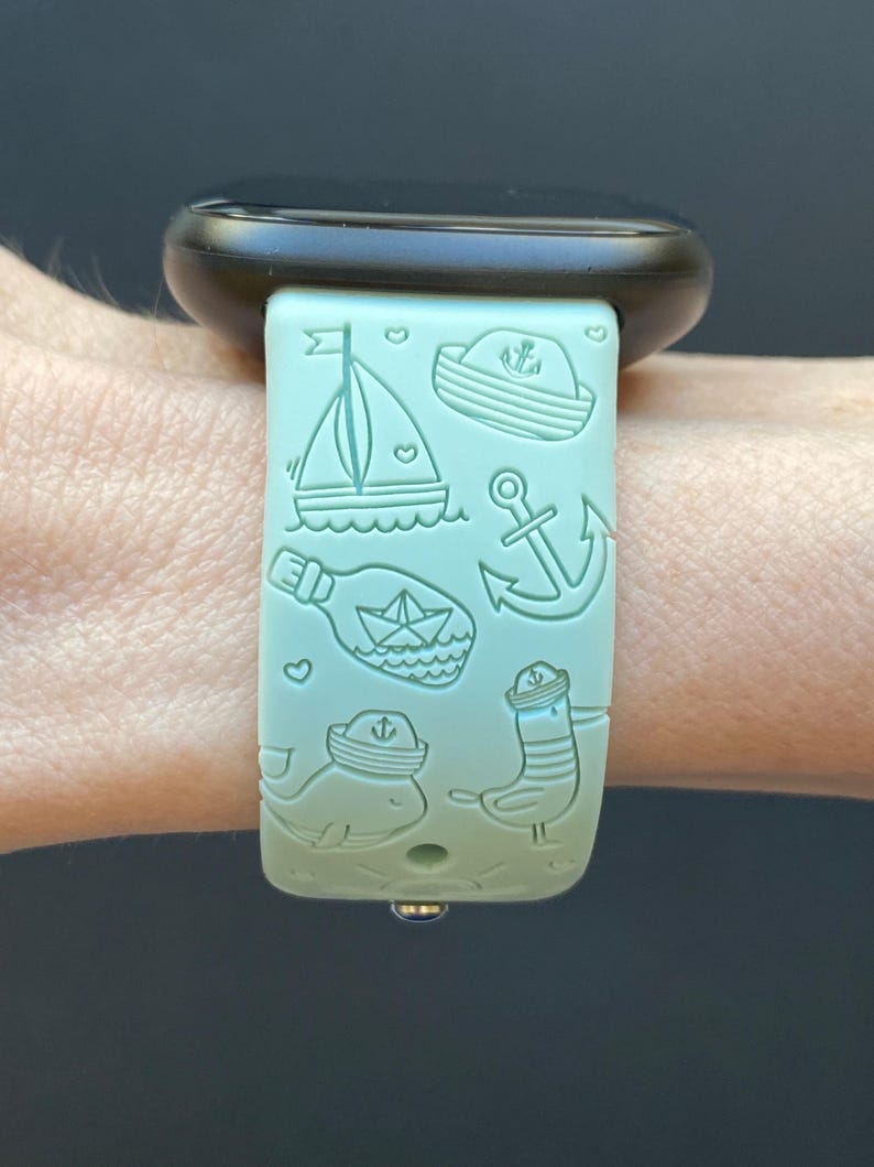 May include: A light blue watch strap with a nautical theme. The strap features a sailboat, an anchor, a bottle with a message in it, a whale, a seagull, and a sailor hat.