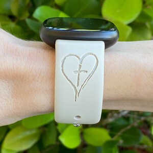 May include: A white silicone watch band with a heart and cross design. The band is worn on a wrist.