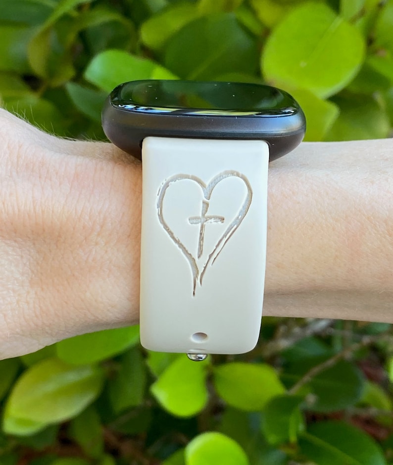 May include: A white silicone watch band with a heart and cross design. The band is worn on a wrist.