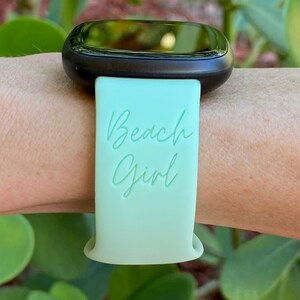 May include: A light green silicone watch strap with the text "Beach Girl" in white lettering.