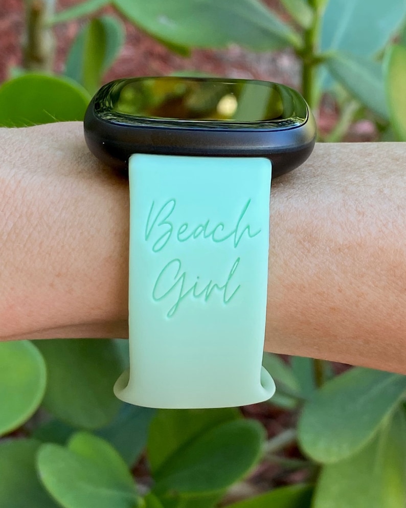 May include: A light green silicone watch strap with the text "Beach Girl" in white lettering.