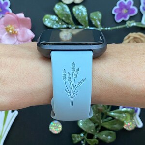 以下が含まれることがあります： 薄い青色のスマートウォッチバンドに、繊細なラベンダーのデザインが施されています。バンドはシリコン製で、滑らかな仕上がりです。