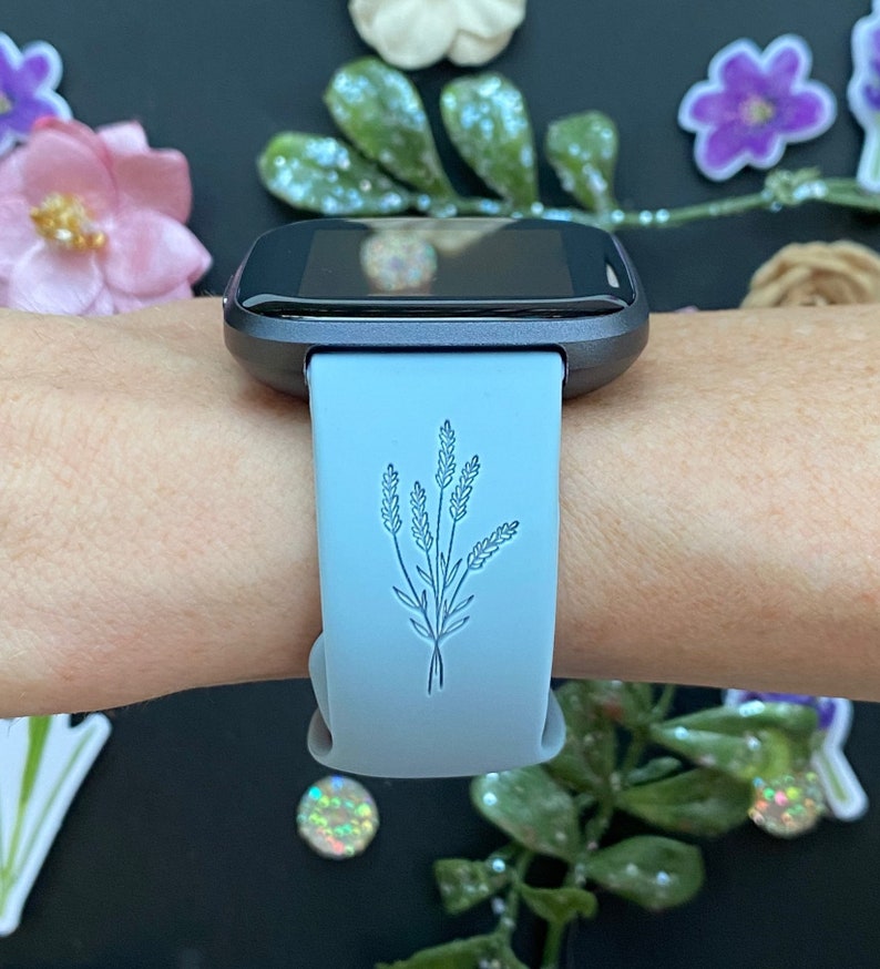 以下が含まれることがあります： 薄い青色のスマートウォッチバンドに、繊細なラベンダーのデザインが施されています。バンドはシリコン製で、滑らかな仕上がりです。