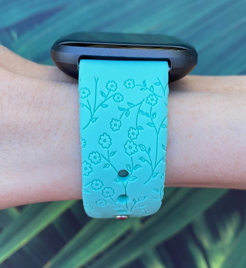 May include: A turquoise blue watch band with a floral pattern. The band is made of silicone and has a textured surface.