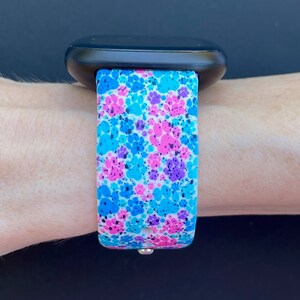 Pu&ograve; includere: Un cinturino per orologio bianco con un motivo a forma di impronta di zampa in blu, rosa e viola. Il cinturino &egrave; realizzato in silicone ed &egrave; compatibile con la maggior parte degli smartwatch.
