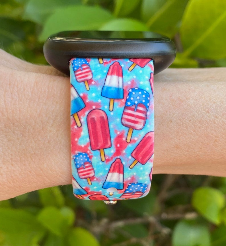 May include: A blue and red patterned watch band with a design of ice cream pops with American flag colors. The band is made of silicone and is compatible with smartwatches.