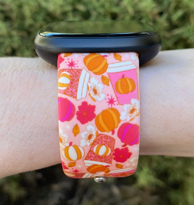 May include: A pink and orange patterned watch band with a design of pumpkins, coffee cups, and flowers. The band is made of silicone and is compatible with smartwatches.