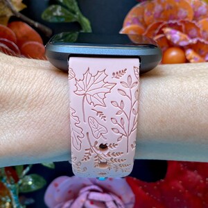 May include: A pink silicone watch band with a floral pattern. The band has a raised design of leaves and flowers.