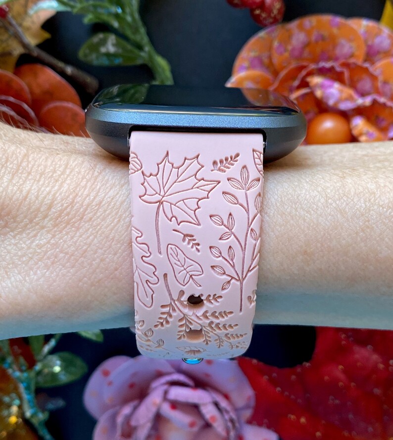 May include: A pink silicone watch band with a floral pattern. The band has a raised design of leaves and flowers.