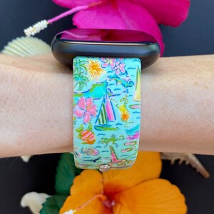 K&ouml;nnte beinhalten: Ein t&uuml;rkisfarbenes Armband f&uuml;r eine Smartwatch mit einem tropischen Muster mit Palmen, Segelbooten, Blumen und Cocktails. Das Armband ist aus Silikon und hat ein schwarzes Zifferblatt.
