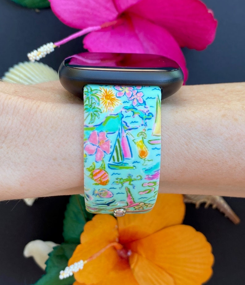 K&ouml;nnte beinhalten: Ein t&uuml;rkisfarbenes Armband f&uuml;r eine Smartwatch mit einem tropischen Muster mit Palmen, Segelbooten, Blumen und Cocktails. Das Armband ist aus Silikon und hat ein schwarzes Zifferblatt.