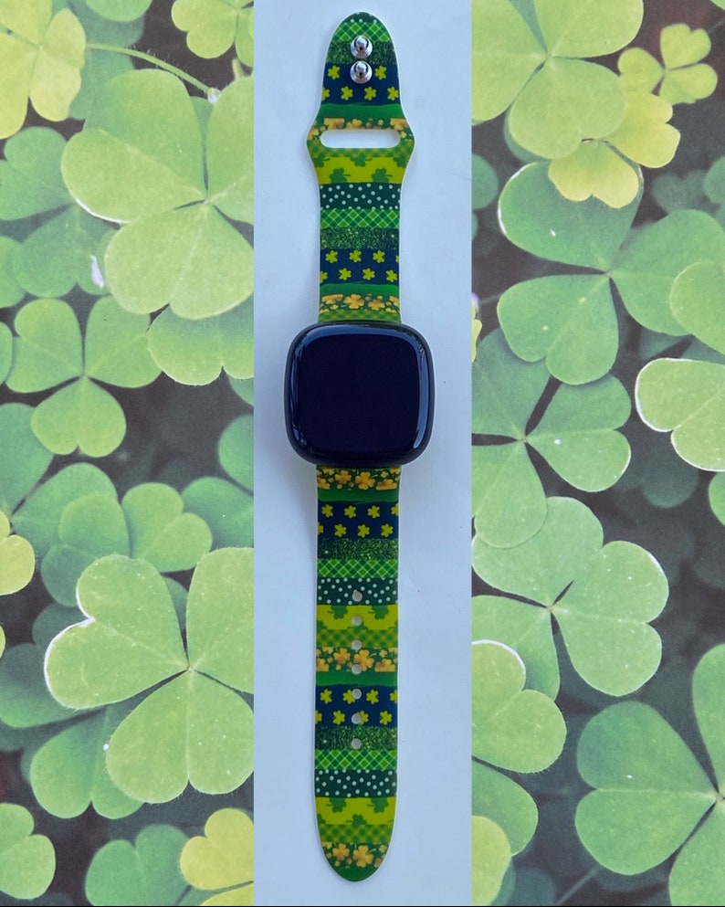 May include: A green and yellow patterned watch band with shamrock designs. The band is made of silicone and has a black watch face.