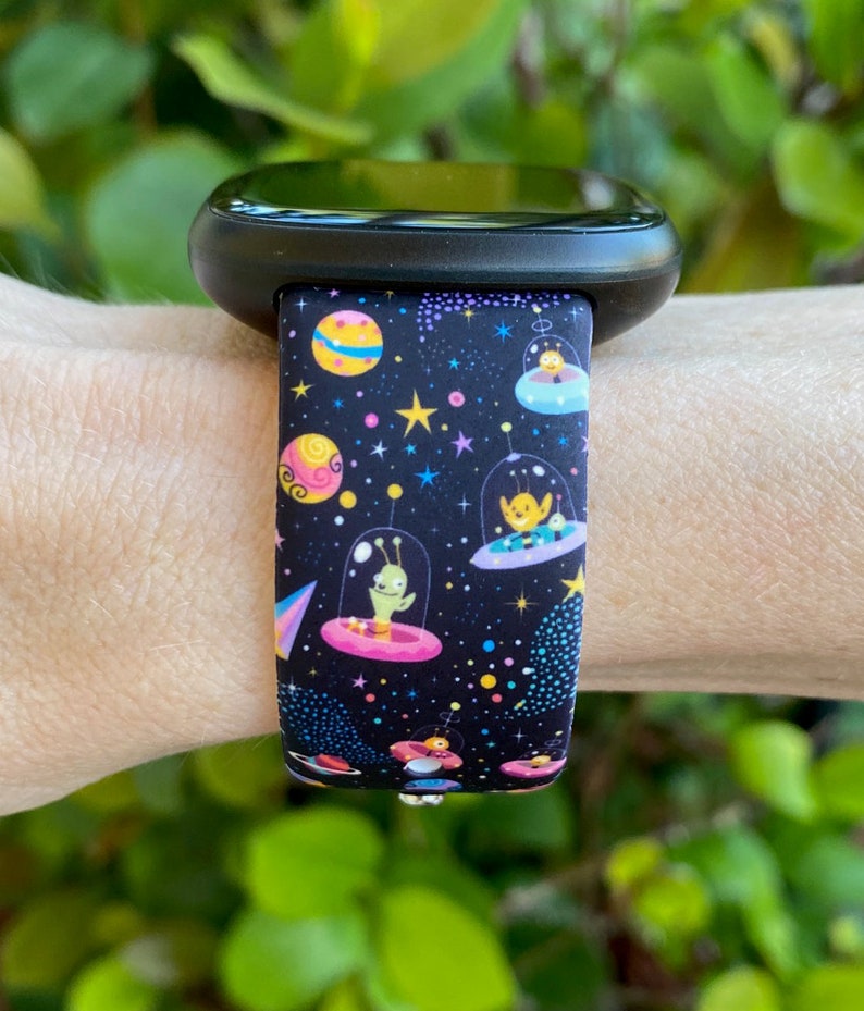 May include: Black watch band with a colorful space-themed print featuring aliens in flying saucers, stars, and planets.