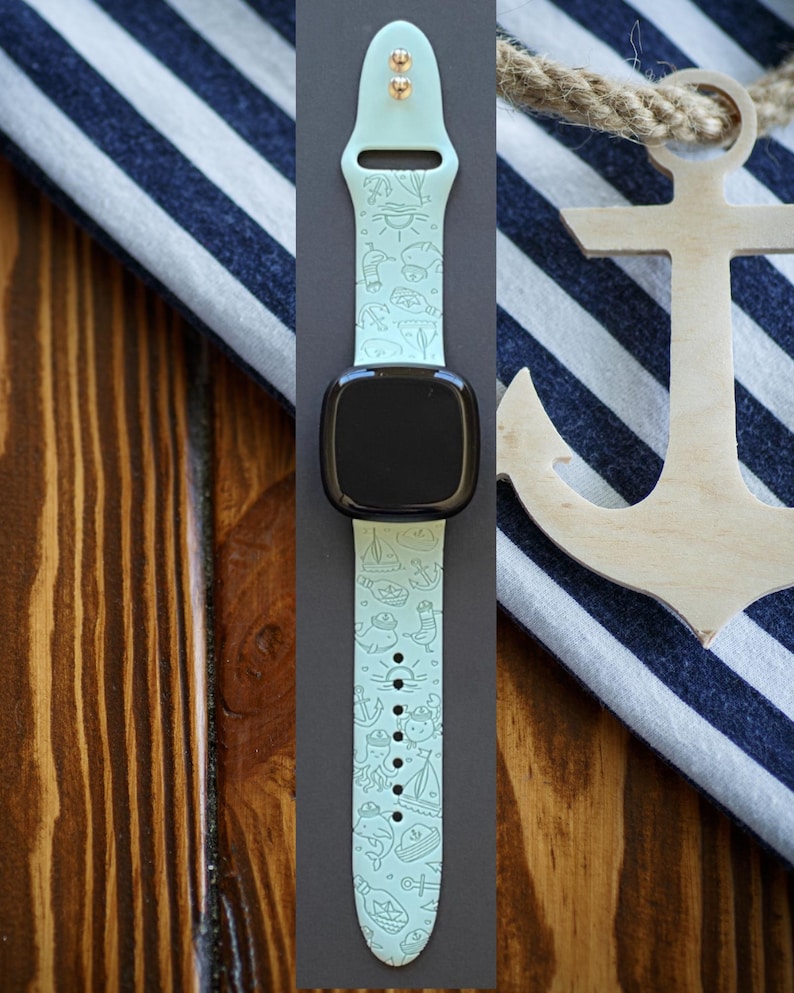 May include: A light blue watch strap with a white anchor and other nautical themed designs. The strap is made of silicone and has a gold buckle.