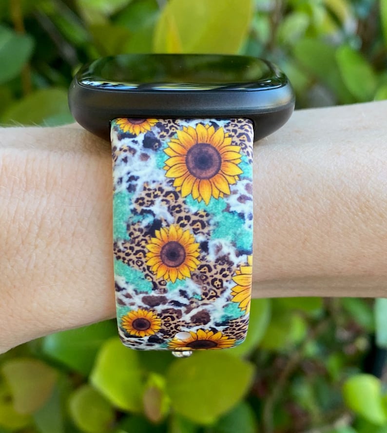 May include: A black smartwatch with a patterned band featuring yellow sunflowers, brown leopard spots, and turquoise accents. The band is attached to the watch face, showcasing a vibrant floral and animal print design.