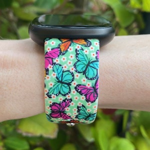 May include: A black smartwatch with a green, white, and pink butterfly patterned band.