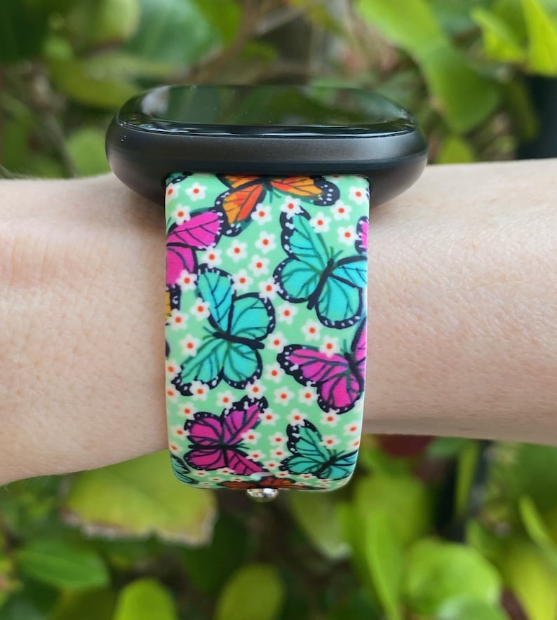 May include: A black smartwatch with a green, white, and pink butterfly patterned band.