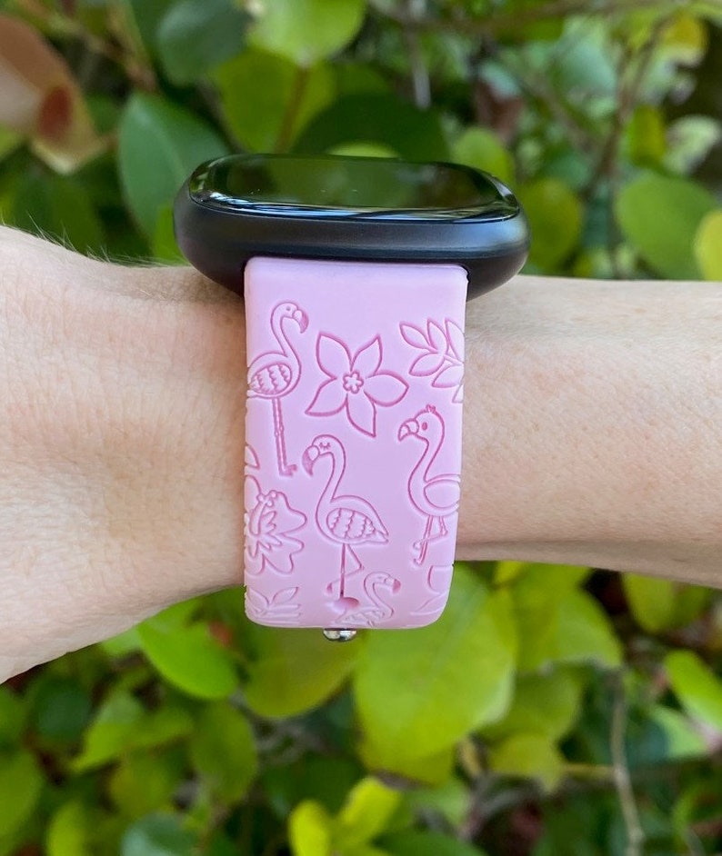 May include: A pink silicone watch band with a flamingo and floral design. The band is compatible with smartwatches.