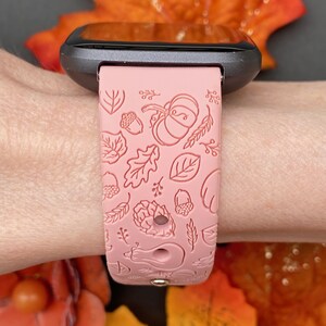 May include: A pink silicone watch band with a fall-themed design. The band features embossed leaves, acorns, pumpkins, and other autumnal elements.