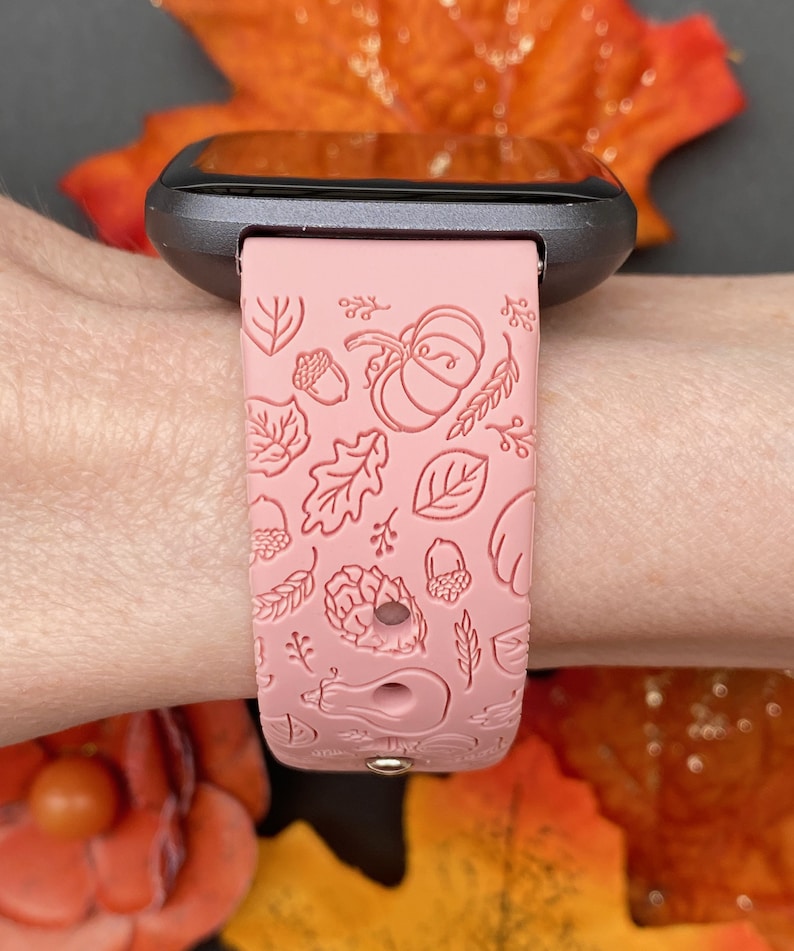 May include: A pink silicone watch band with a fall-themed design. The band features embossed leaves, acorns, pumpkins, and other autumnal elements.