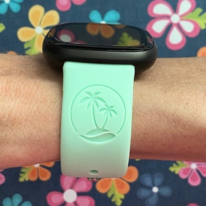 May include: A light green smartwatch band with a palm tree design. The band is made of silicone and has a smooth finish.