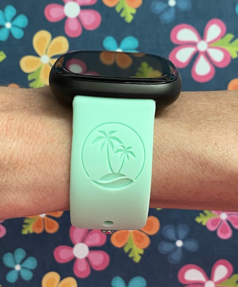 May include: A light green smartwatch band with a palm tree design. The band is made of silicone and has a smooth finish.