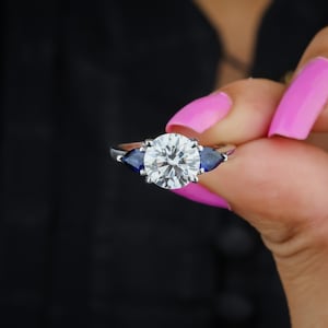 3 CT ラウンドカット モアッサナイト & ブルーペアーサファイア 3 ストーン ツイスト エンゲージリング | ハンドメイド 結婚指輪 | 女性への記念日の贈り物