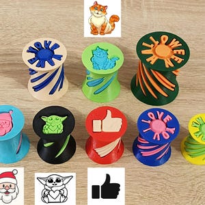 May include: Nine colorful, round, plastic stampers with different designs. The designs include a cat, a thumbs up, a Christmas tree, a baby Yoda, and the words "You Are", "Love You", "Merry Xmas", and "Halloween".