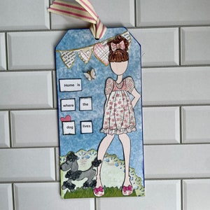 May include: A blue and white paper craft tag with a girl doll, a black poodle, and the text "Home is where the dog lives".