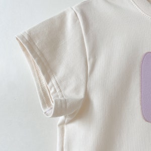 May include: A white short-sleeved t-shirt with a purple patch on the front.